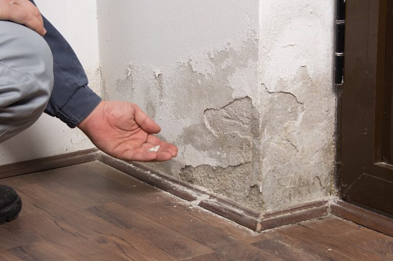 Eine Hand zeigt wie die Wand abbröckelt nach Wasserschaden.